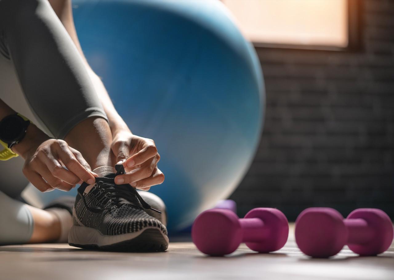 Young sporty woman with smart watch tying shoelaces in fitness