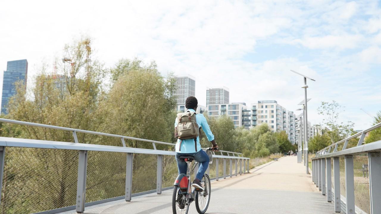 Girl riding a bike across a bridge toward a city.