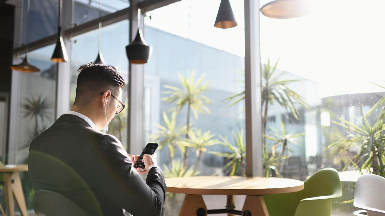 Hombre con traje trabajando desde su teléfono, escuchando música con auriculares